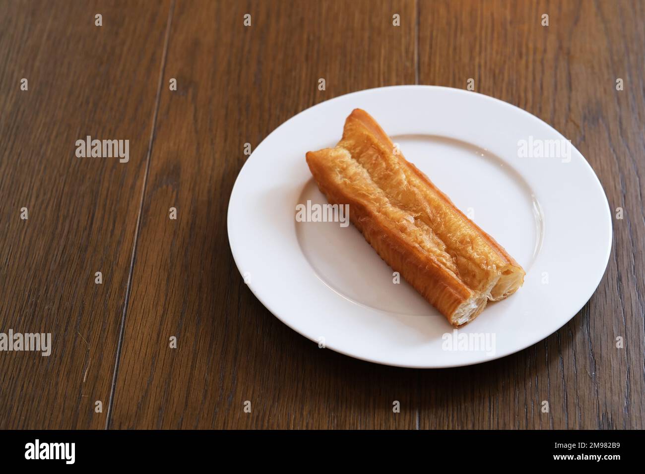 Un morceau de youtiao chinois (bâton de pâte frite) sur une assiette sur une table en bois. En-cas traditionnel pour le petit déjeuner en Chine Banque D'Images