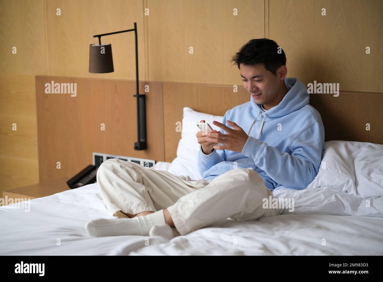 Beau sourire asiatique jeune homme utiliser le téléphone sur le lit Banque D'Images