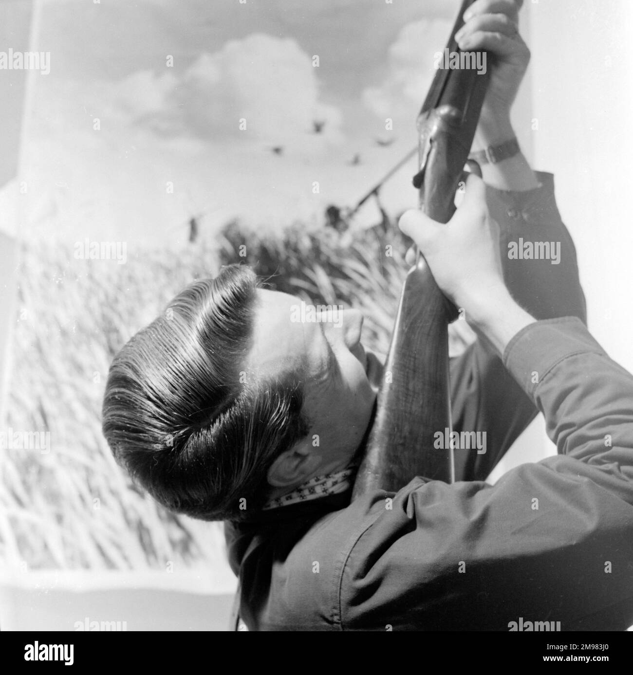 Publicité pour les produits de cheveux Silvikrin -- modèle masculin (Roy Curtis) visant un fusil dans l'air. Banque D'Images
