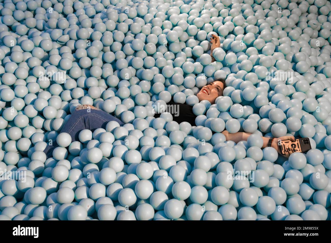 Une femme heureuse jouant dans une piscine remplie de boules bleues en plastique Banque D'Images