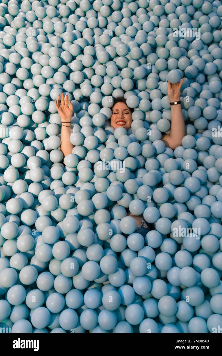 Une femme heureuse jouant dans une piscine remplie de boules bleues en plastique Banque D'Images