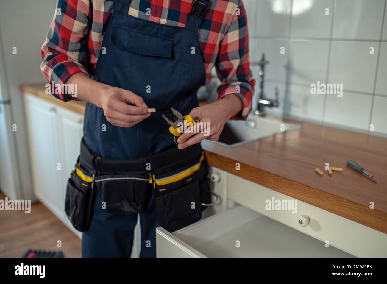 Photo rognée d'un menuisier tenant une paire de pinces et une cheville en bois cannelé dans ses mains Banque D'Images