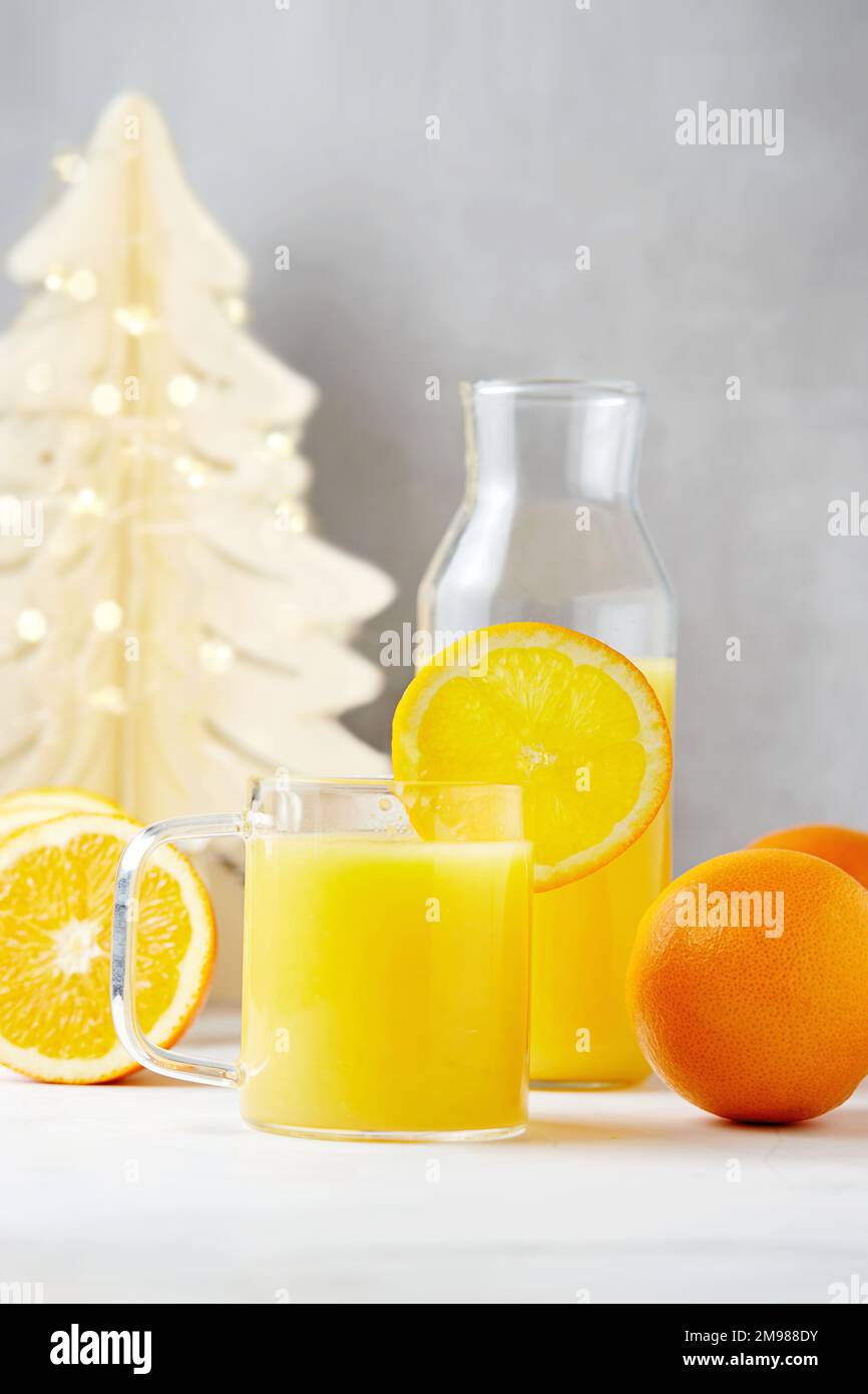 Bouteille et verre de jus d'orange fraîchement pressé avec des oranges fraîches à côté d'une décoration d'arbre de Noël Banque D'Images