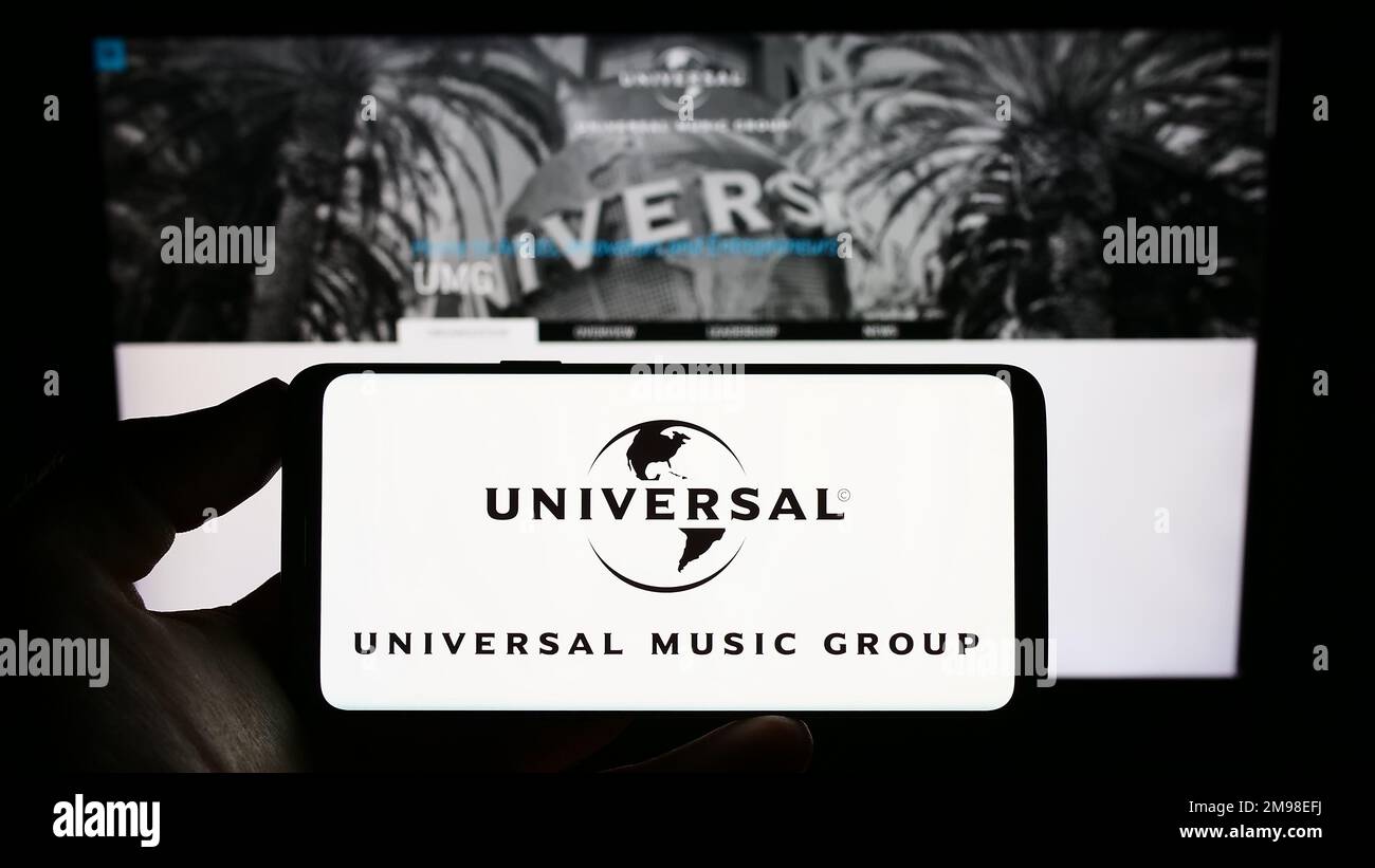 Personne tenant un smartphone avec le logo de la société Universal Music Group N.V. (UMG) à l'écran en face du site Web. Mise au point sur l'affichage du téléphone. Banque D'Images