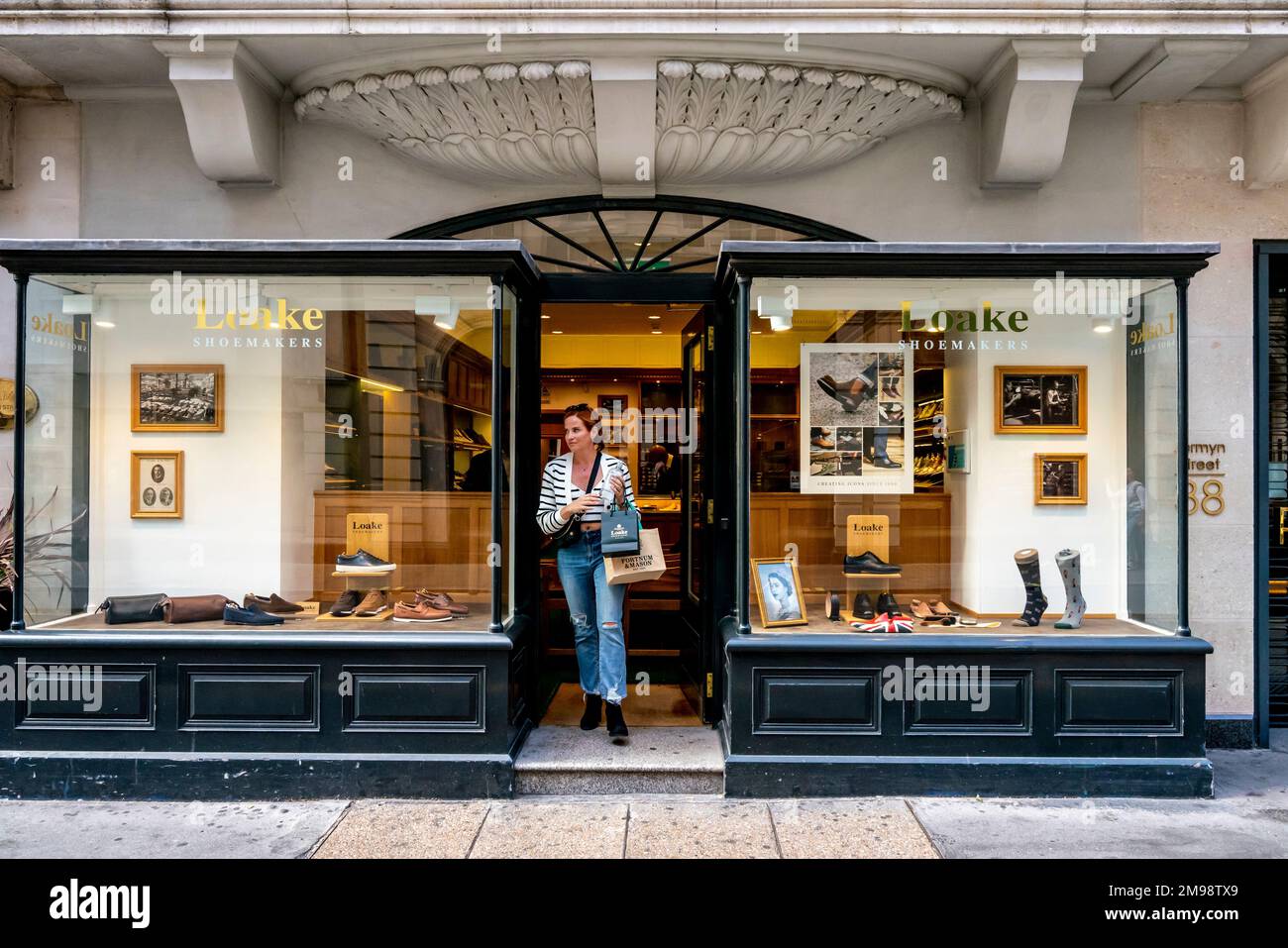 Une jeune femme à la mode quittant les cordonniers de Loake, Jermyn Street, Londres, Royaume-Uni. Banque D'Images