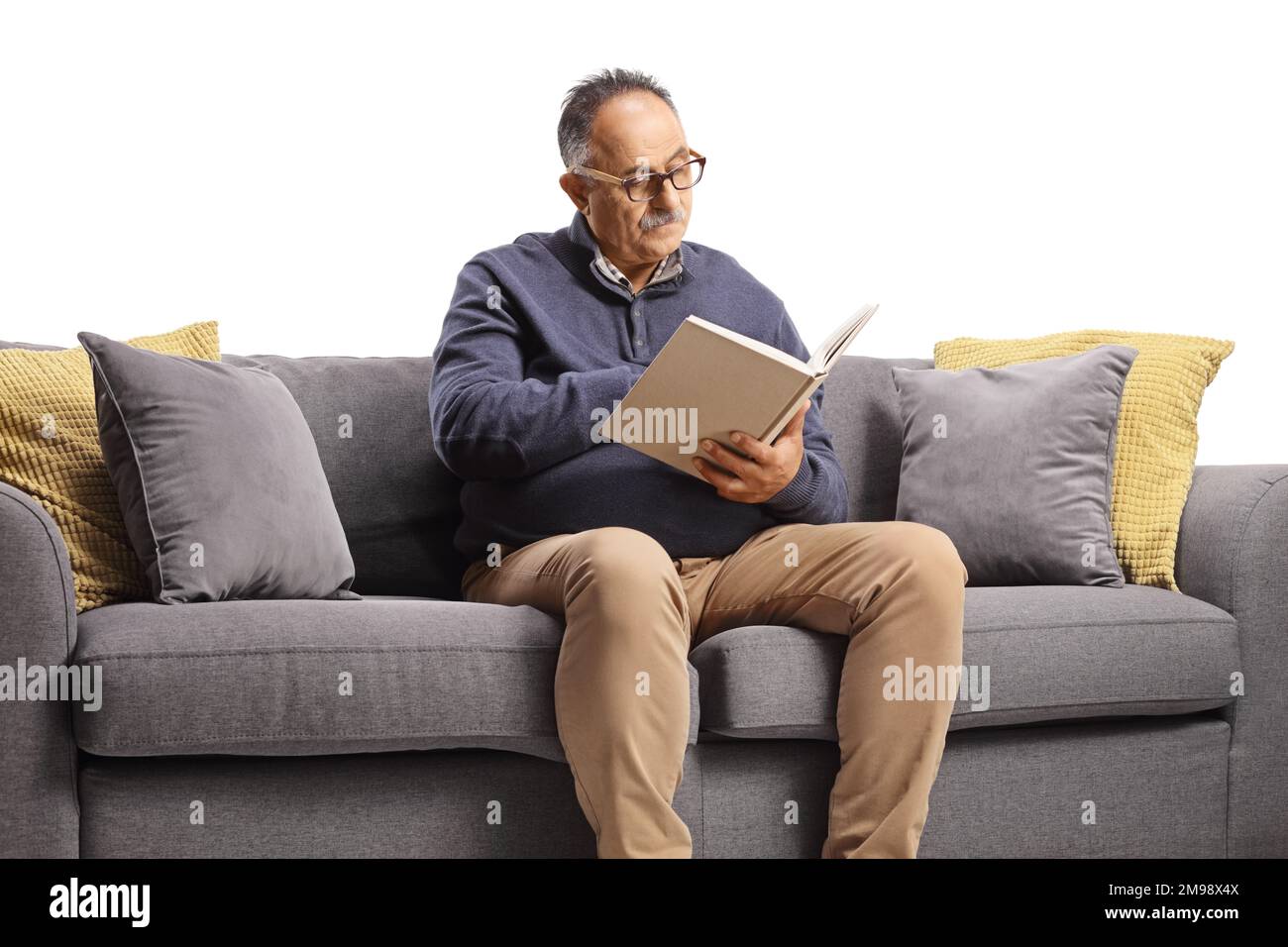 Homme mature assis sur un canapé et lisant un livre isolé sur fond blanc Banque D'Images
