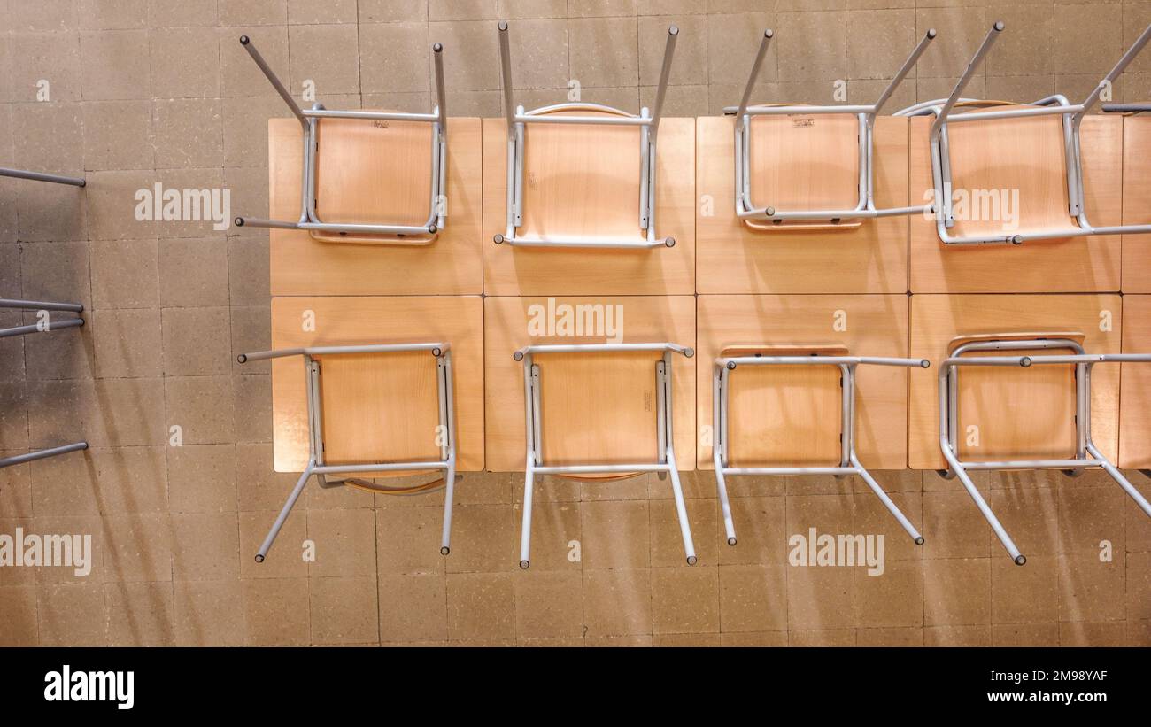 Vue de dessus de chaises similaires à l'envers placées sur une table en bois dans une salle de classe légère après les cours Banque D'Images