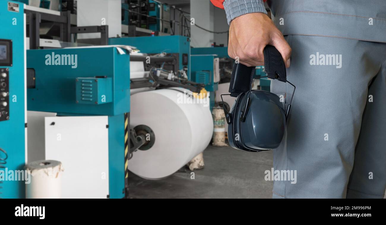 Homme avec protections auditives travaillant dans une imprimerie avec une machine à imprimer Banque D'Images