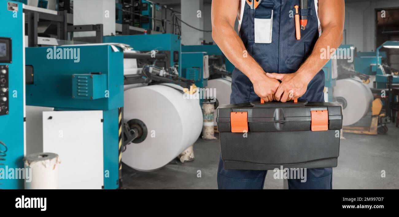 Homme avec boîte à outils travaillant dans une imprimerie avec une machine à imprimer Banque D'Images