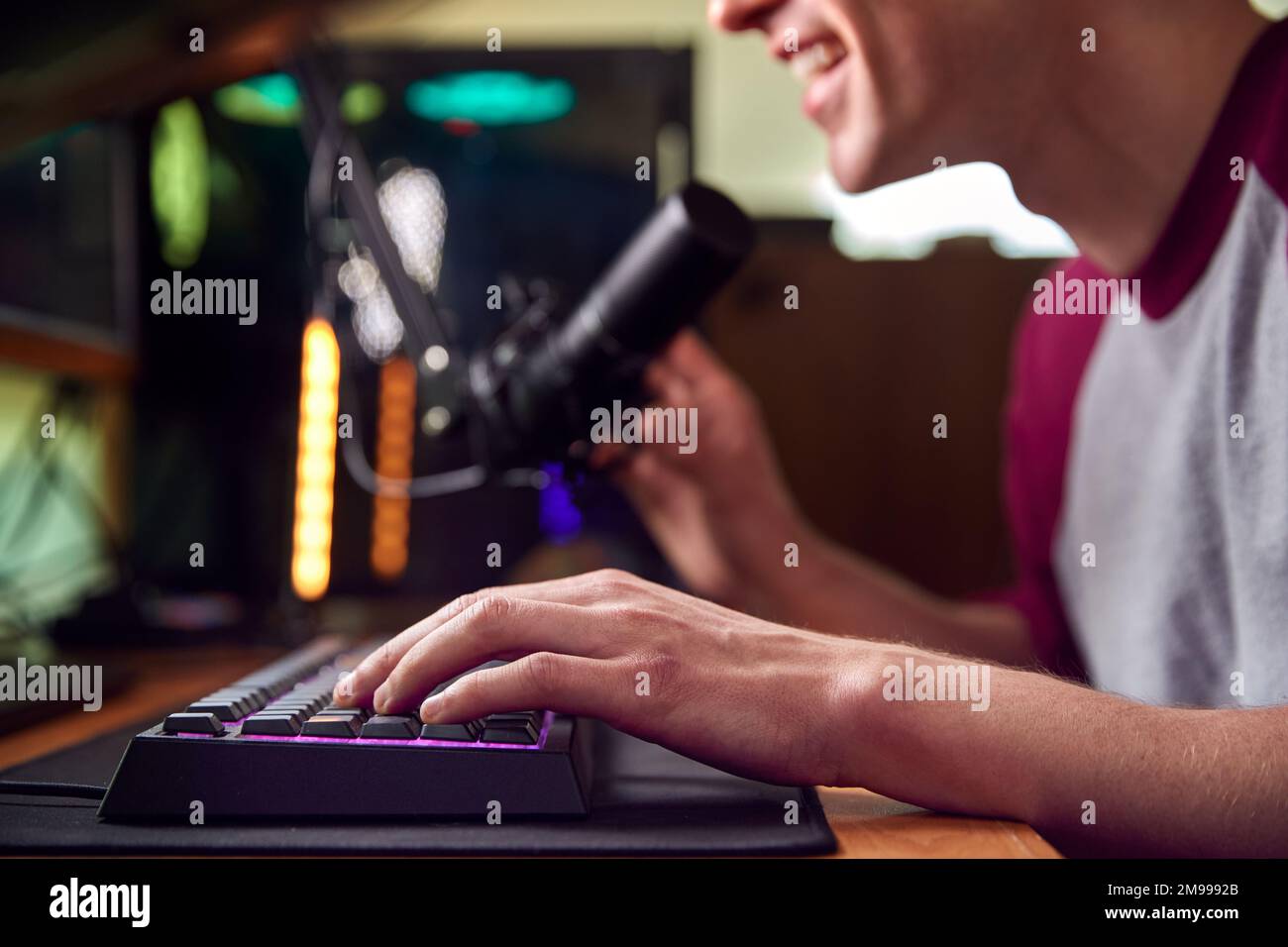 Gros plan des mains sur le clavier comme l'homme Jeux à la maison assis au bureau avec plusieurs moniteurs Banque D'Images