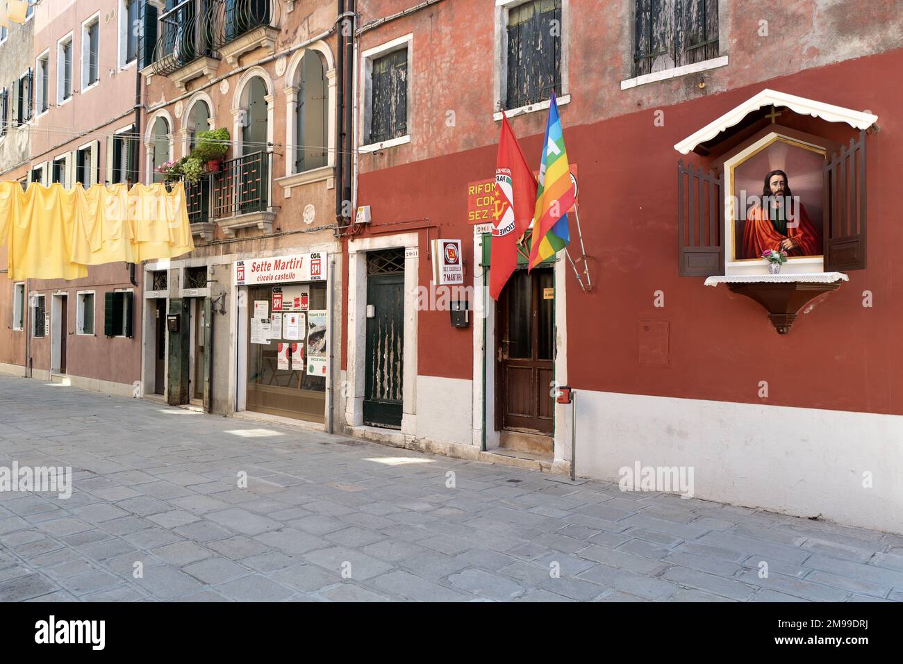 Feuilles jaunes accrochées sur une ligne pour se sécher, à côté par un club communiste et une chapelle de Jésus-Christ sur le mur. Banque D'Images