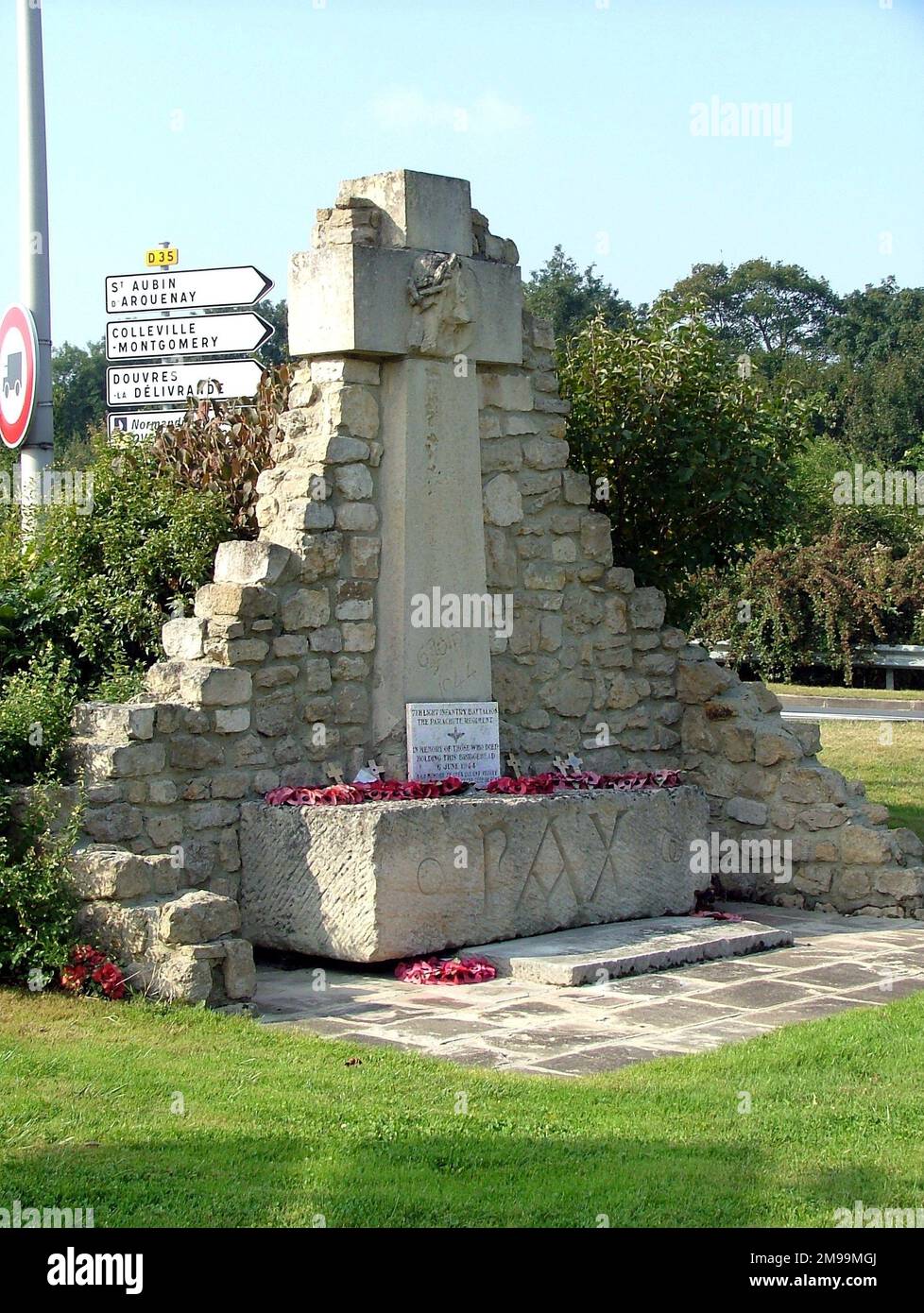 Ce monument religieux en pierre, qui se trouve en face de Benouville Mairie, porte l'inscription PAX en bas et est confronté à une plaque commémorant les par Le 7th devait être renforcé pour les premiers arrivants, les hommes de John Howard à Pegasus Bridge, mais ils étaient dispersés par de forts vents. Cependant, ils ont été ralliés par le bugler qui était arrivé avec l'OC, le colonel Lt Pine-Coffin. Banque D'Images