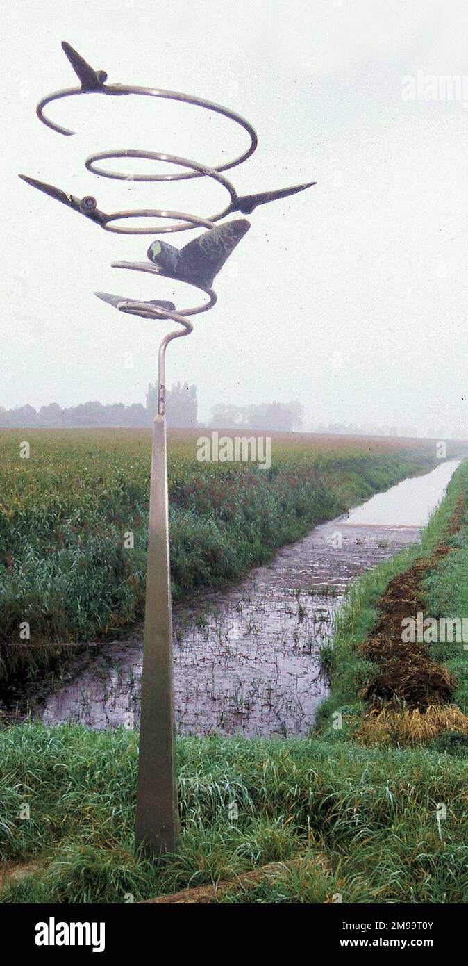 La piste d'atterrissage ici, dans les anciens forelands des Maas à Keent, a été faite par les Allemands comme un terrain d'atterrissage d'urgence, mais n'a jamais été utilisé par eux. Toutefois, le 26 septembre 1944, 209 C47 Dakotas du Commandement du transporteur de la 52nd escadre ont atterri à Keent avec des troupes et des fournitures pour les Américains et l'Armée britannique de 2nd. Malgré le sol marécageux et soggy, la bande a continué d'être utilisée par les escadrons de chasseurs de 2nd forces aériennes tactiques. Le mémorial distinctif montrant des avions qui volent d'un ressort en spirale comme s'ils tournaient autour de la piste d'atterrissage, a été conçu par Albert Sanders. À droite du métal M Banque D'Images