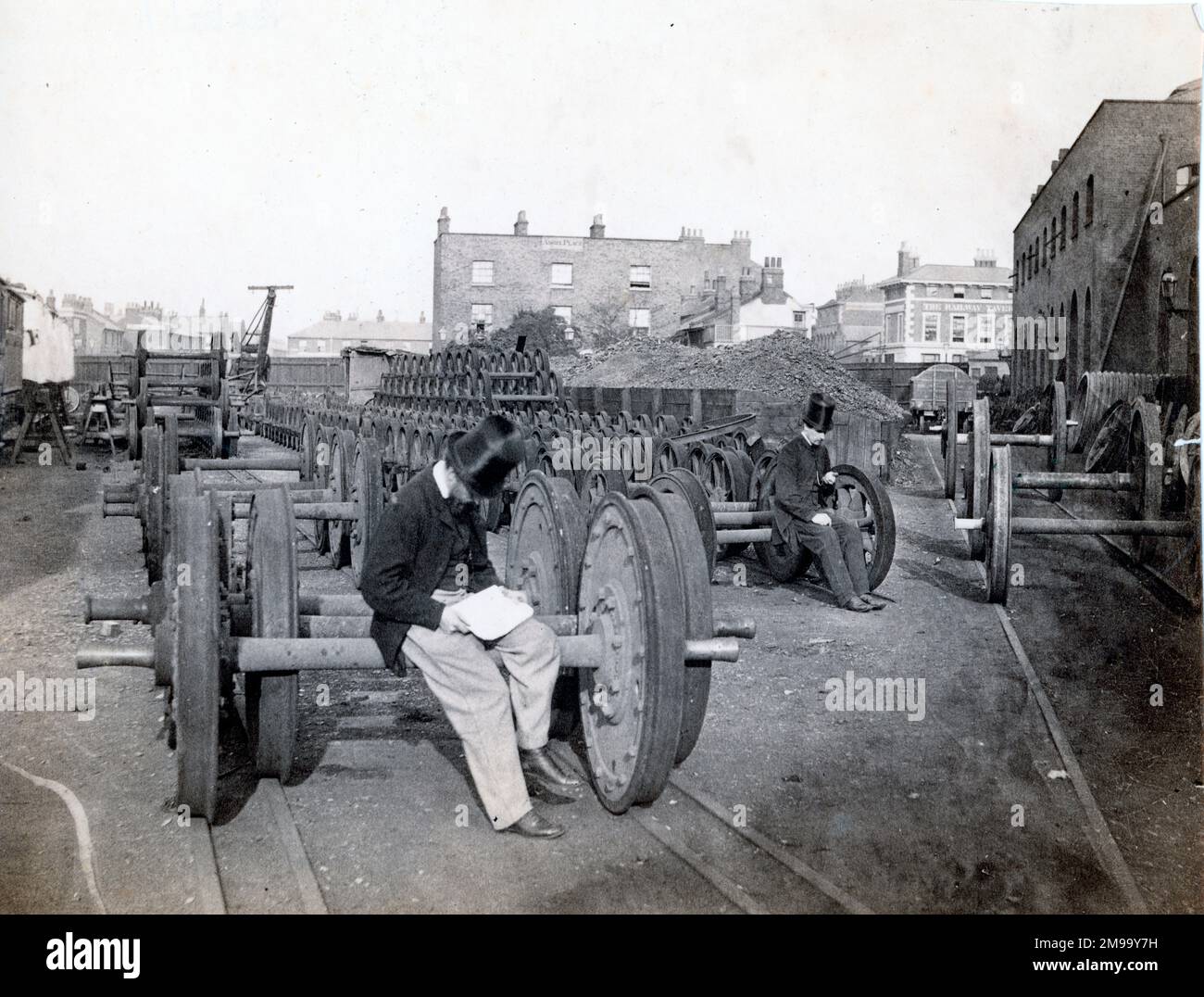 Une vue sur le côté nord de la locomotive du Great Eastern Railway travaille à Stratford (Londres est) le 1864 mai avec William Henry Maw, alors chef du bureau de dessin, assis sur l'essieu d'un train de roues de chariot ou de chariot, avec son collègue James Kitson plus en arrière. En arrière-plan se trouve la maison publique de la Taverne ferroviaire (qui est encore existante) et les habitations dans la région d'Angel place. Banque D'Images