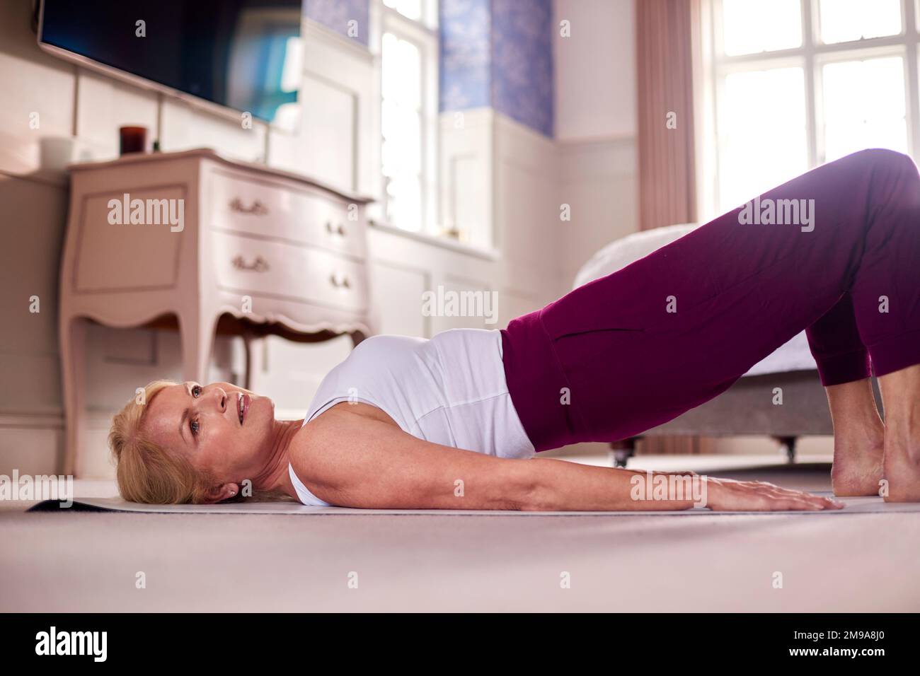 Femme active mature faisant de l'exercice de yoga sur Mat à la maison Banque D'Images
