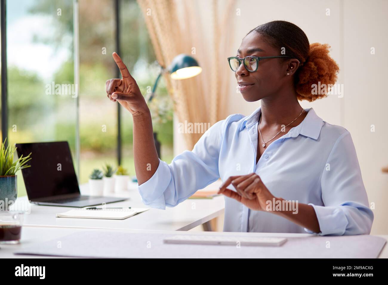 Femme travaillant à domicile assis au bureau en interaction avec la technologie AR ou VR Banque D'Images