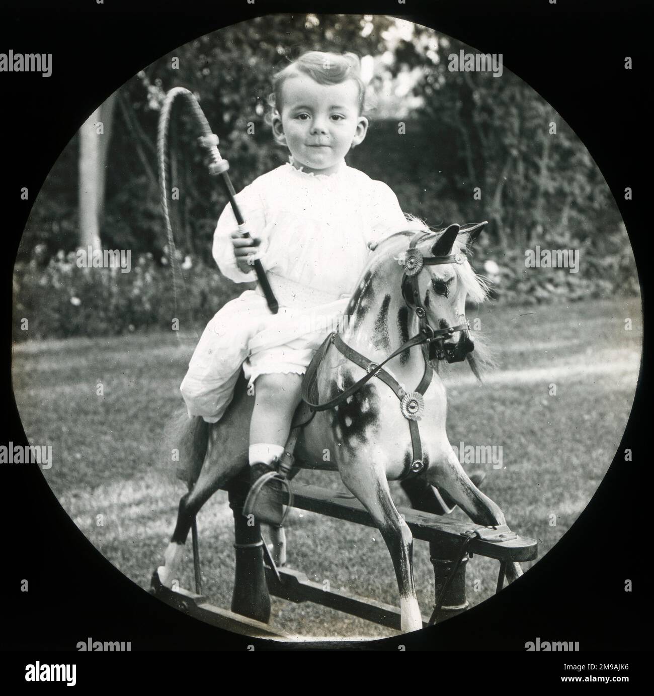 Petit garçon sur un cheval à bascule avec fouet jouet. Banque D'Images