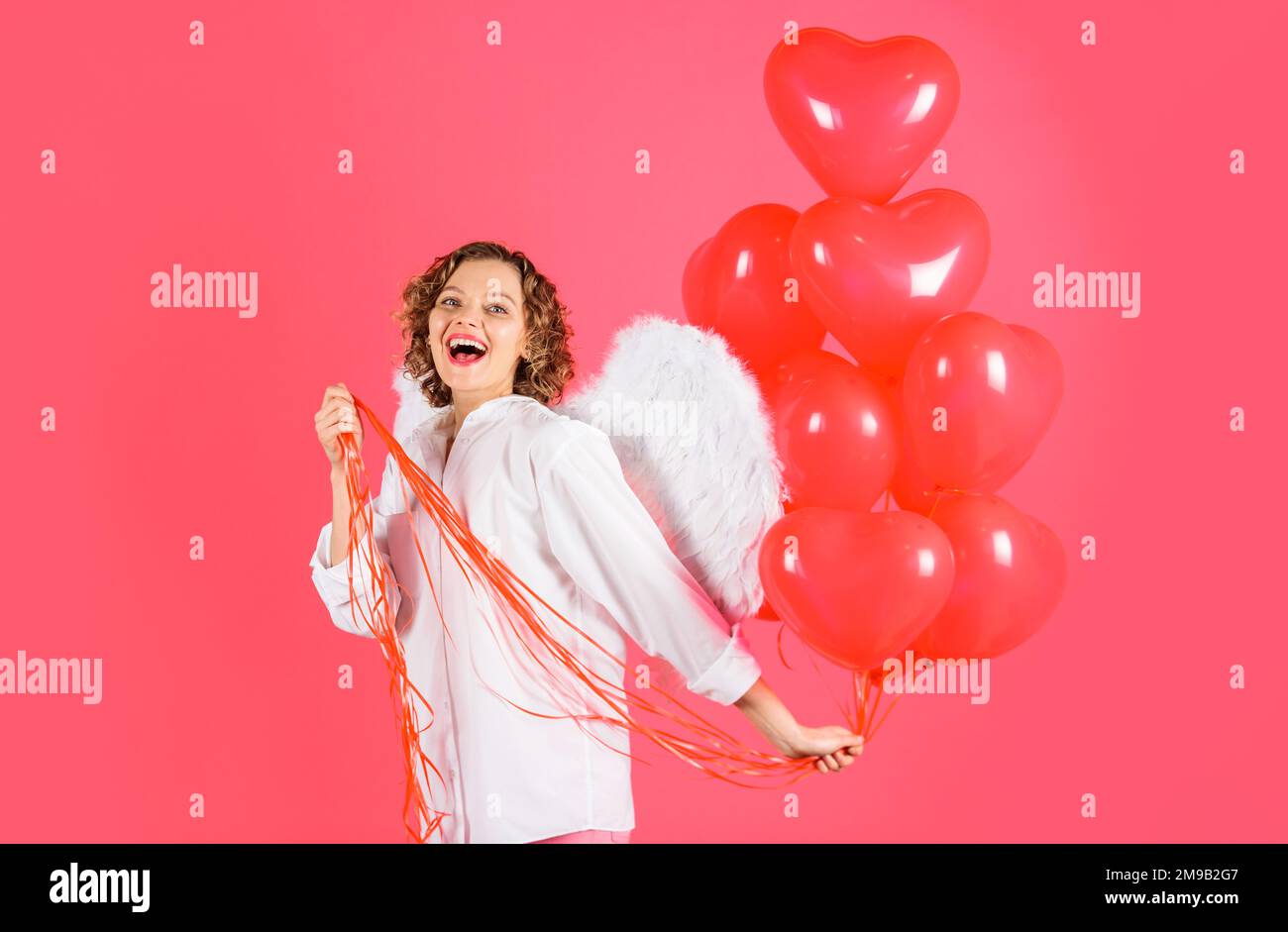 Fête de la Saint-Valentin. Ange féminin avec ballons rouges à coeur. Femme heureuse avec des ailes d'anges. Banque D'Images