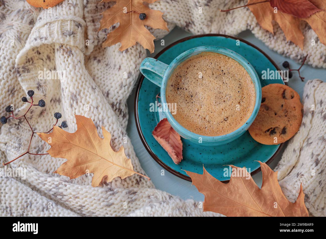 Écharpe tricotée blanche, tasse de café bleue, biscuits et feuilles jaunes sèches Banque D'Images