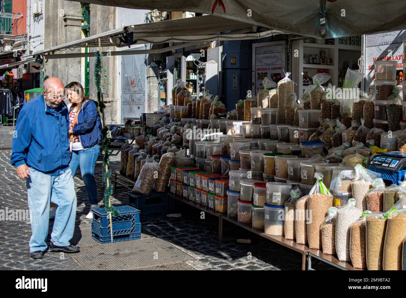 Un homme passe devant un stand de rue vendant des légumineuses et des herbes sèches et des épices dans la banlieue de Sanita, Naples, Italie Banque D'Images