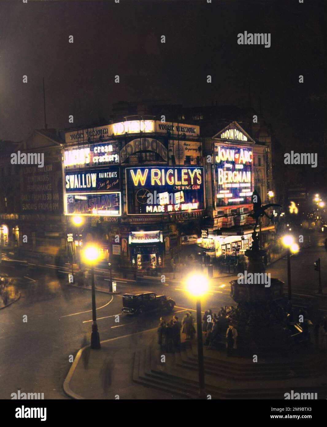 Piccadilly Circus et la statue d'Eros la nuit. Le lettrage éclairé brille, annonçant Votrix Vermouth, Jacob's Cream crackers, Swallow imperméable, et Wrigley's chewing Gum. Le Pavillon de Londres montre Jeanne d'Arc avec Ingrid Bergman. Banque D'Images