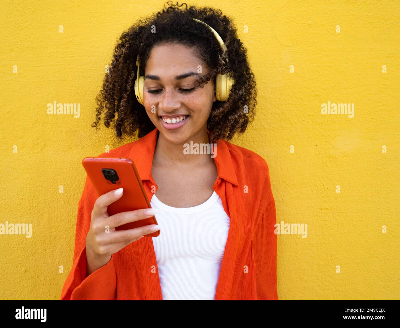 Une jeune femme joyeuse parle avec un téléphone portable sur un mur jaune dans la ville Banque D'Images