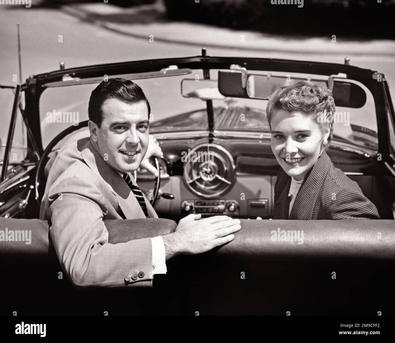 1950S HOMME ET FEMME SOURIANTS ASSIS SUR LE SIÈGE AVANT DE LA VOITURE TRANSFORMABLE TOURNÉ VERS LES ÉPAULES ET LE SIÈGE ARRIÈRE À L'APPAREIL PHOTO - M3495 HAR001 HARS FEMMES PERSONNES HOMMES B&W PARTENAIRE GAI ET SOURIRES DEVENU DES FEMMES JOYEUSES JEUNE HOMME ADULTE JEUNE FEMME ADULTE NOIR ET BLANC RACE BLANCHE HAR001 ANCIENNE Banque D'Images