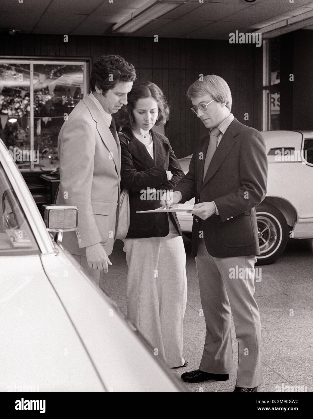 1970S HOMME ET FEMME DANS LA CONCESSION DE VOITURE DISCUTANT AVEC LE VENDEUR EN ALLANT AU-DESSUS DES SPÉCIFICATIONS ET DES PRIX - M9755 HAR001 STYLE HARS COMMUNICATION INFORMATION SUR LE VÉHICULE SHOWROOM STYLE DE VIE FEMMES EMPLOIS MARIÉS MONTRANT CONJOINT MARI ESPACE DE COPIE PLEINE LONGUEUR FEMMES MI-LONGUEUR CONCESSIONNAIRES PERSONNES ACHÈTENT AUTOMOBILE HOMMES CONCESSIONNAIRE TRANSPORT B&W PARTENAIRE SHOPPER SHOPPERS COMPÉTENCE RÊVES PROFESSION VENDRE COMPÉTENCES AVENTURE SERVICE À LA CLIENTÈLE SEDAN AUTOS OPPORTUNITÉ OCCUPATIONS ACHAT AUTOMOBILES VÉHICULES ADULTE MOYEN ADULTE HOMME ADULTE MOYEN-ADULTE FEMME VENTESHOMMES FEMMES NOIR ET BLANC RACE BLANCHE HAR001 OLD FASHIONED Banque D'Images