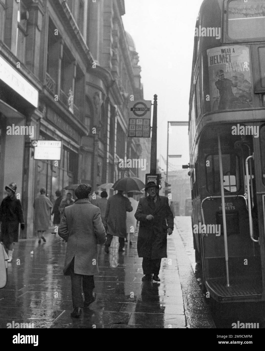Ce vieil homme, qui attend un arrêt de bus londonien sous la pluie, semble être sur le point de sauter à bord du bus Routemaster qui vient d'arriver. Banque D'Images