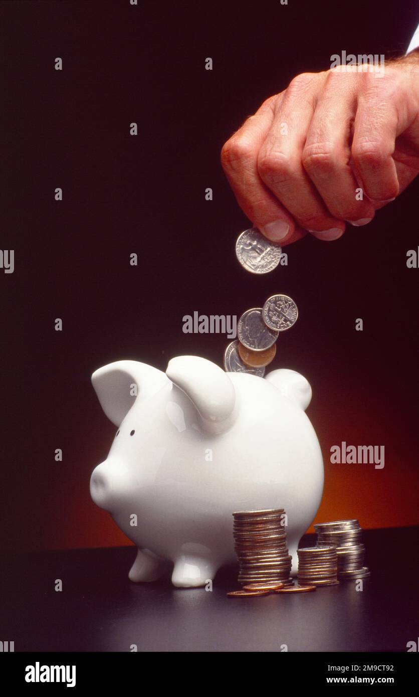 Gros plan d'une main mâle alimentant des pièces de monnaie dans une banque de porc Banque D'Images