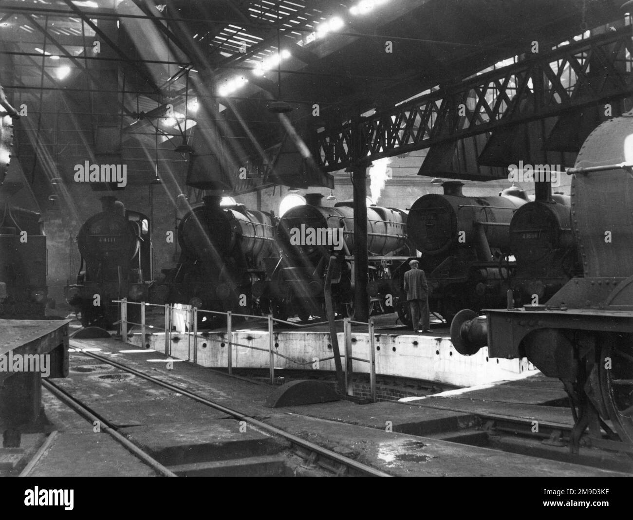 Homme dans un hangar de chemin de fer plein de locomotives à vapeur. Banque D'Images