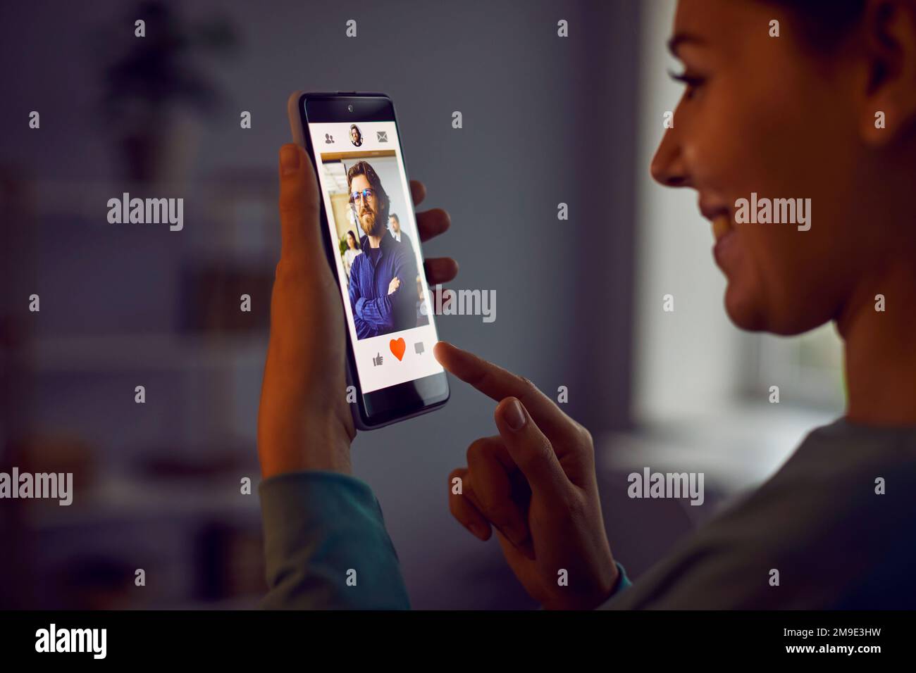 Une femme gaie appuie sur le bouton rouge coeur sur le profil de l'homme qu'elle aime dans l'application de datation. Banque D'Images