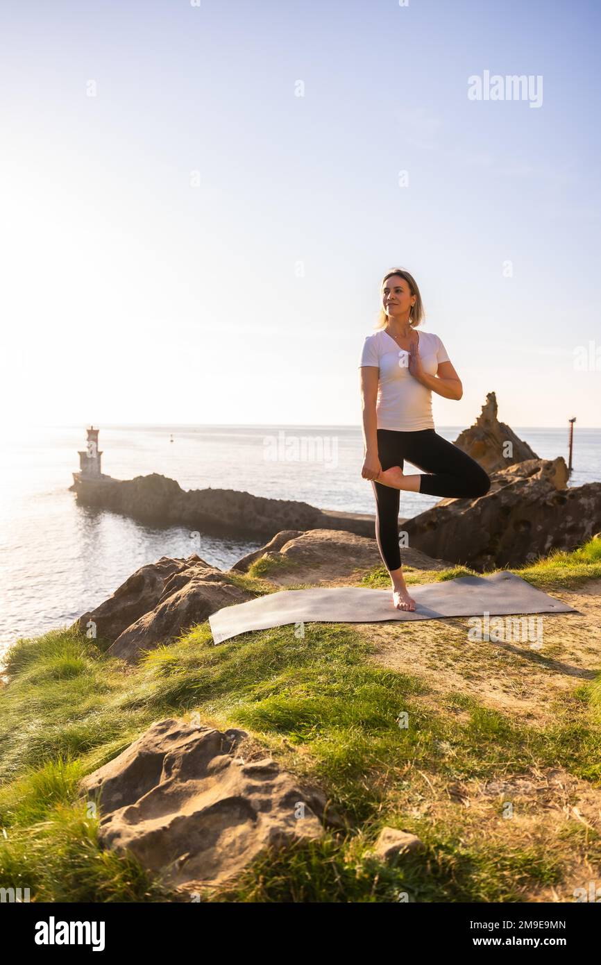 Une femme blonde faisant des exercices de yoga dans la nature au bord de la mer, s'étendant à côté d'un phare, la vie saine et naturiste, pilates à l'extérieur Banque D'Images