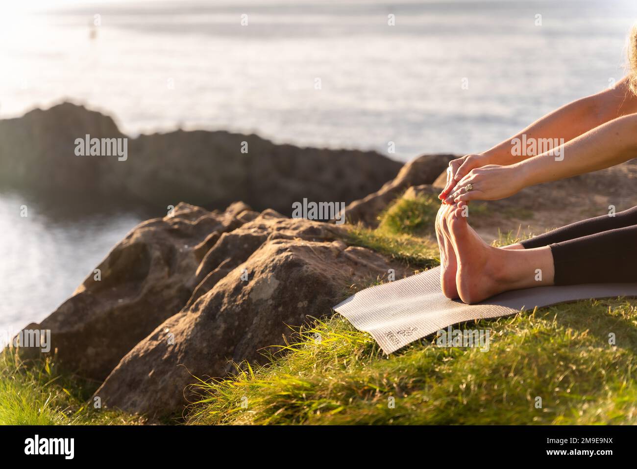 Pieds d'une femme faisant des exercices de yoga dans la nature au bord de la mer, s'étendant à côté d'un phare, la vie saine et naturiste, pilates en plein air Banque D'Images
