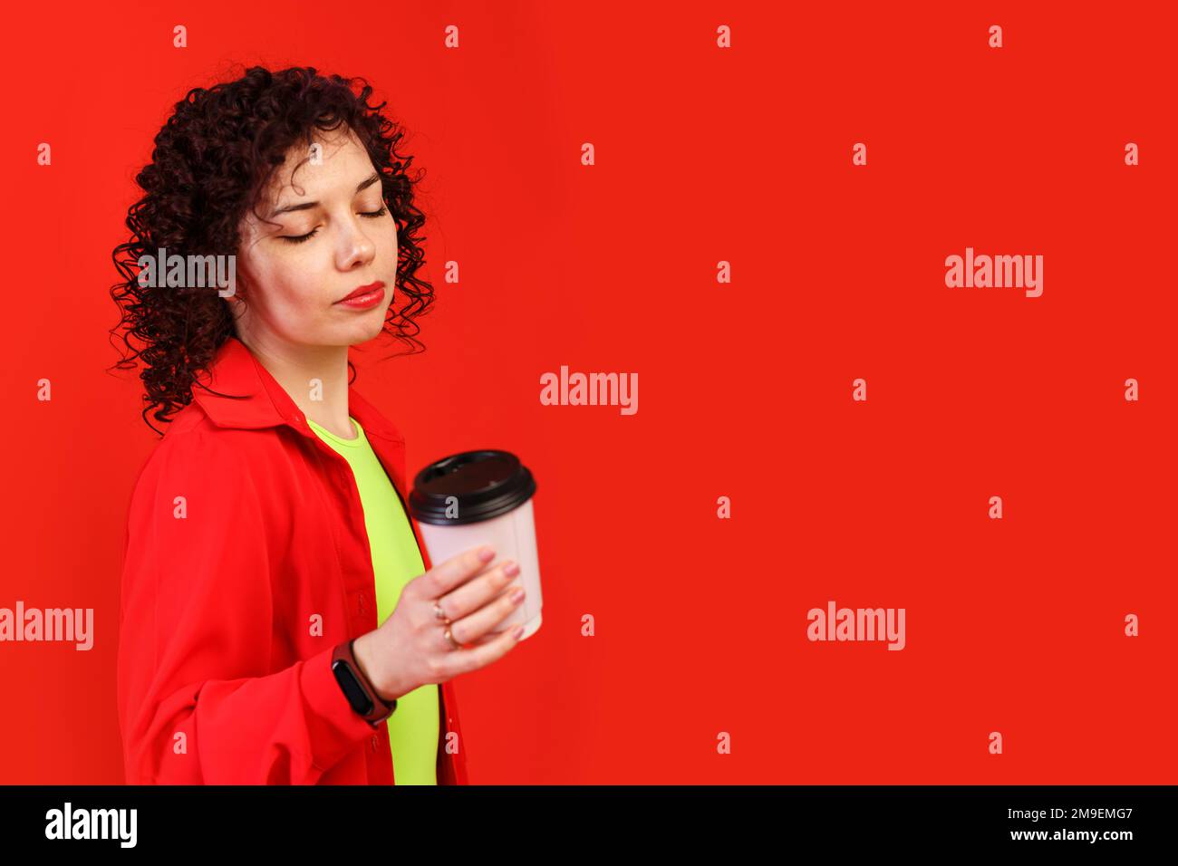 Une jeune femme romantique tient une tasse de papier rose avec du café ou du thé. Fille en rouge vif et t-shirt jaune. Isolé sur fond rouge Banque D'Images