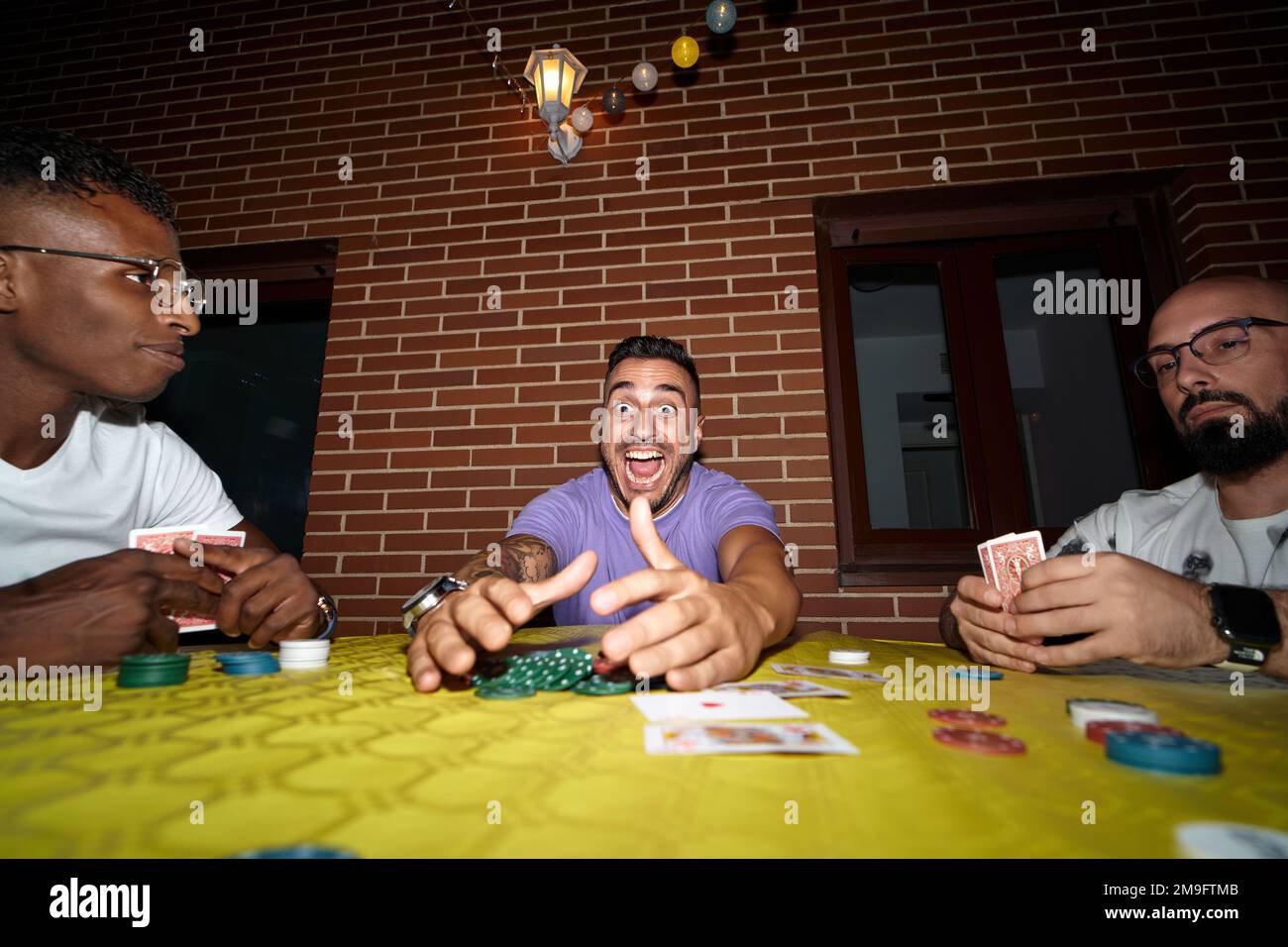 L'homme heureux et excité gagne dans le jeu de cartes de poker tout en jouant avec des amis. Banque D'Images