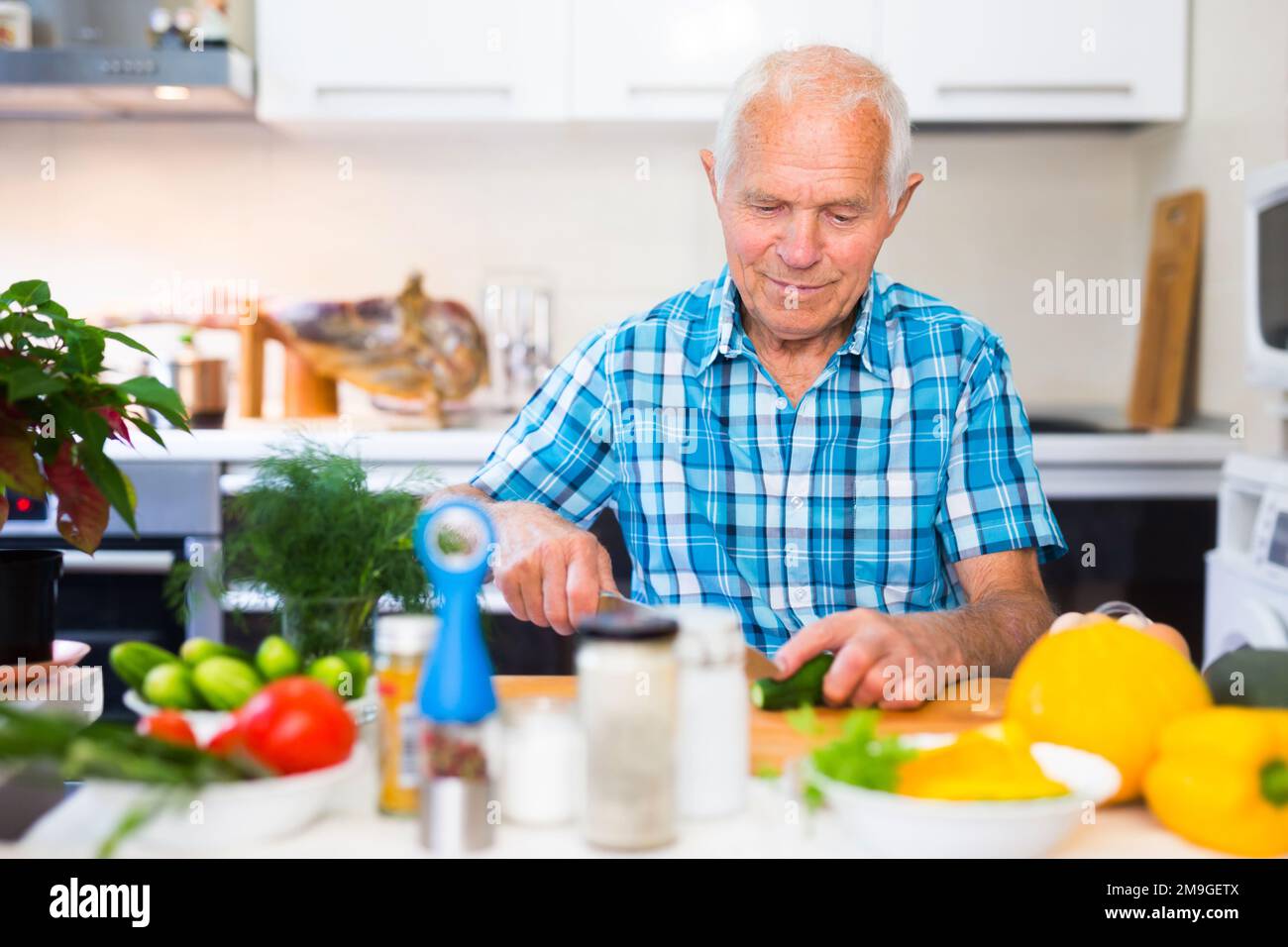 un homme âgé coupe des légumes pour les salades à la table de la cuisine Banque D'Images