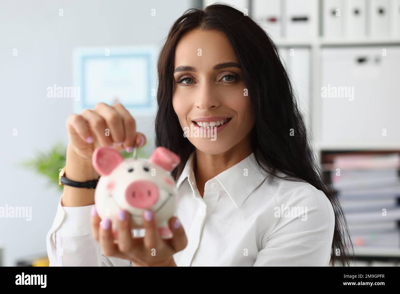 Portrait d'une femme souriante jetant de la monnaie dans une banque de piggy Banque D'Images