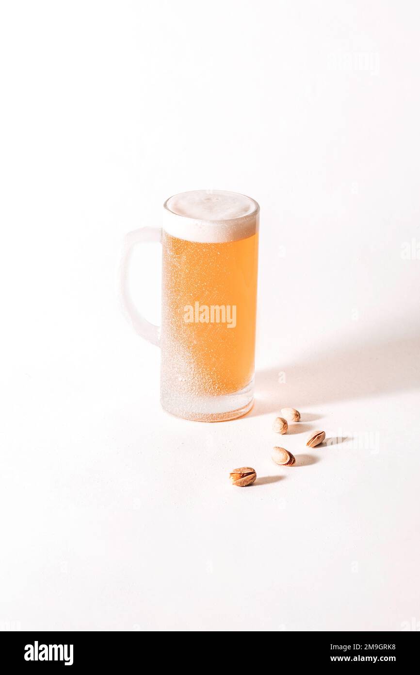 Tasse à bière fraîche avec givre sur la surface et mousse à l'intérieur sur fond blanc, Pistachios Banque D'Images