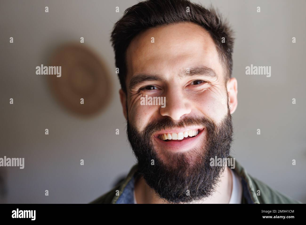 Portrait en gros plan d'un beau jeune homme biracial barbu souriant contre un mur blanc, espace de copie Banque D'Images