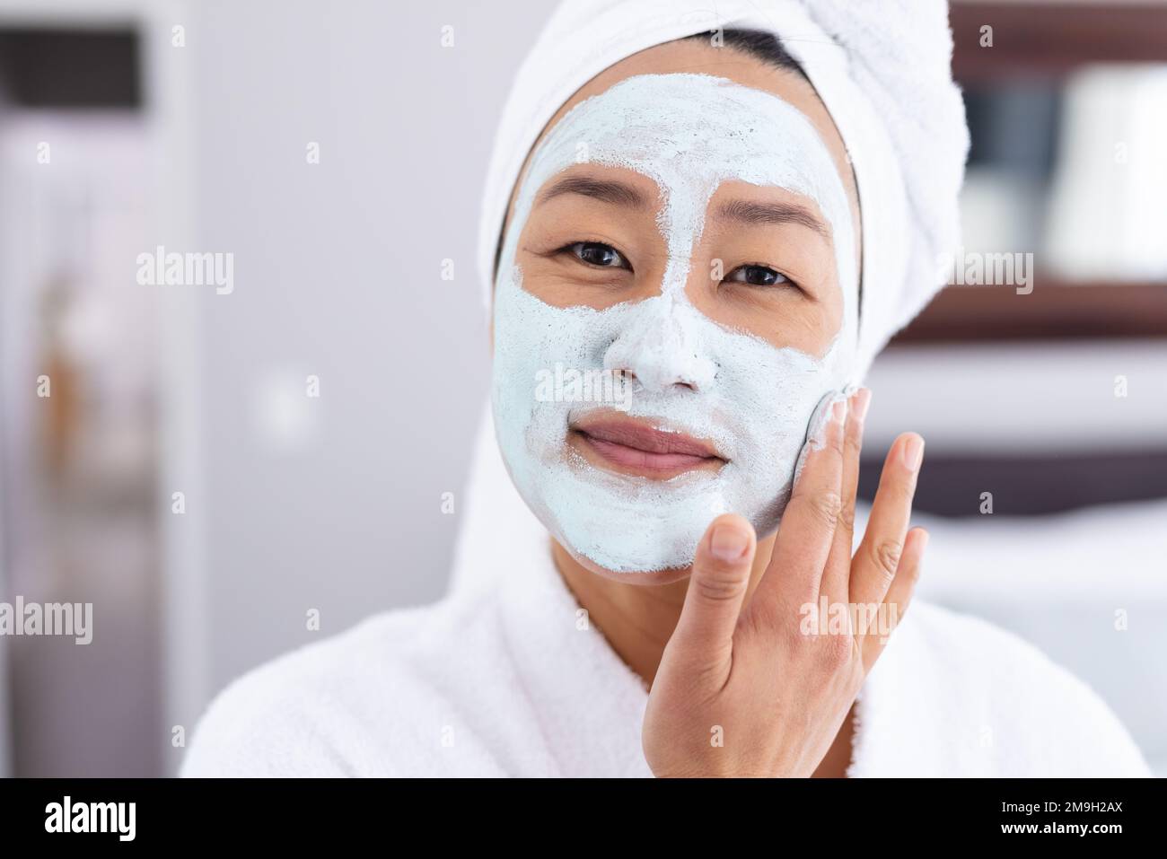 Portrait d'une femme asiatique heureuse appliquant un masque de beauté dans la salle de bains Banque D'Images
