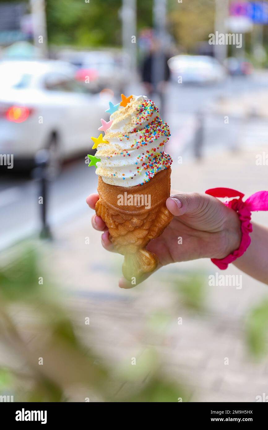 Gros plan vertical d'une main tenant un cône taiyaki avec de la crème glacée et de la saupoudrer Banque D'Images