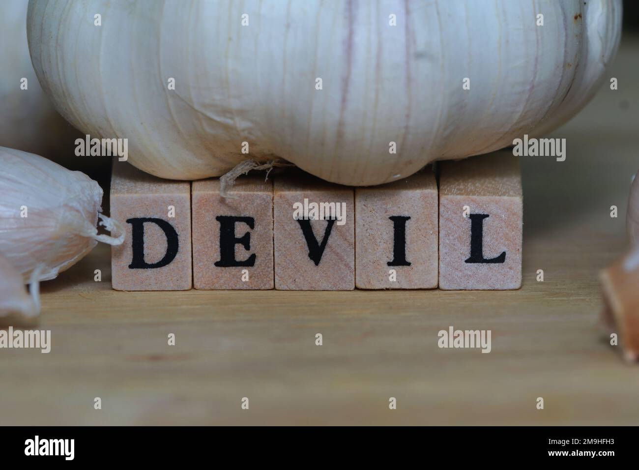 Un gros plan de l'ail avec le mot « Devil » fait avec des cubes en bois isolés sur une planche à découper en bois Banque D'Images