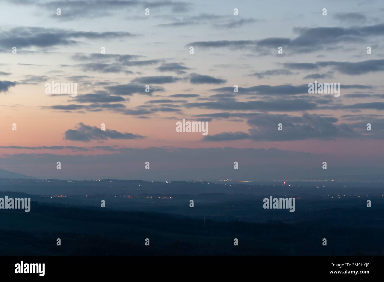 Zones claires dans la campagne sombre au crépuscule, paysage vallonné et ciel nuageux Banque D'Images