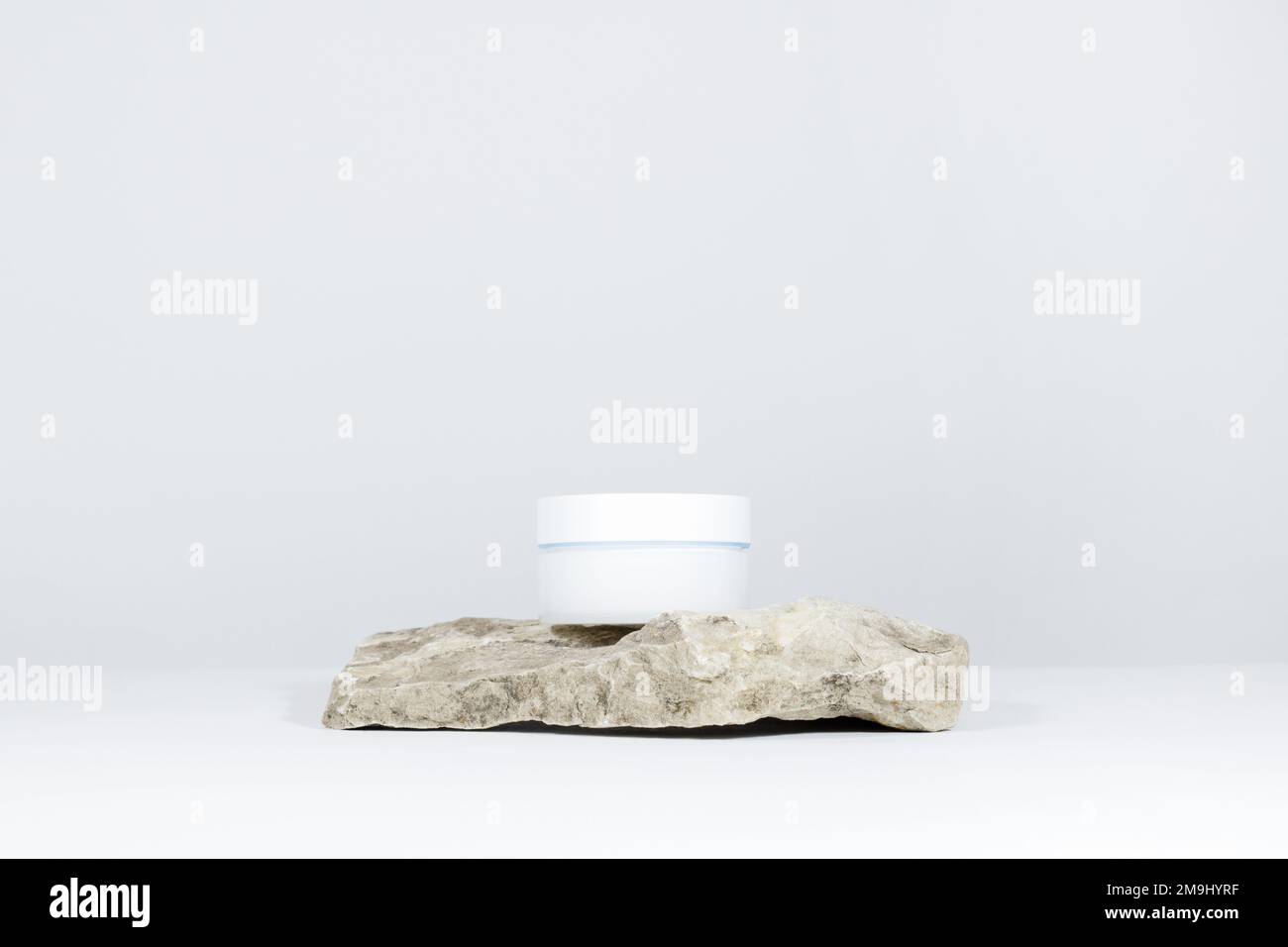 Une maquette de pot blanc de crème sur un piédestal en pierre naturelle, sur une table blanche, avec des ombres dures. Design élégant du produit, identité. Banque D'Images