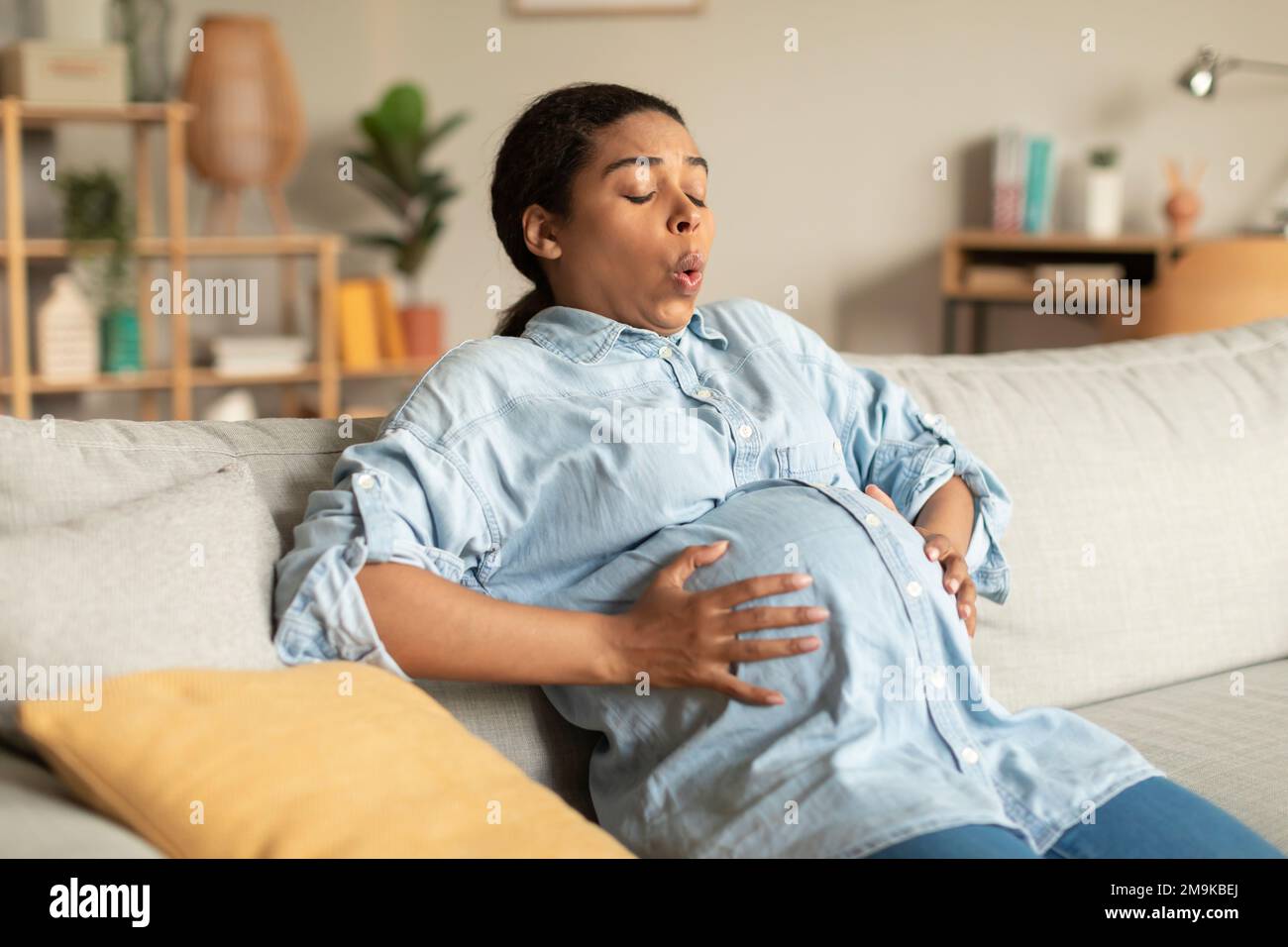 Femme enceinte afro-américaine touchant le ventre, souffrant de contractions douloureuses et faisant des exercices de respiration Banque D'Images
