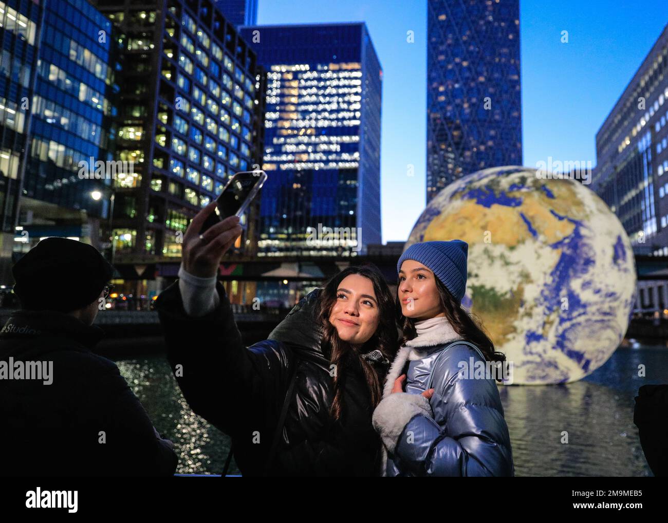 Londres, Royaume-Uni. 18th janvier 2023. Deux jeunes femmes prennent des selfies. Floating Earth de Luke Jerram, situé dans Middle Dock, est une installation globe géante de 10 mètres qui vise à créer un sentiment de l'« effet de vue d'ensemble » ressenti par les astronautes. Il s'avère populaire auprès des visiteurs qui prennent des selfies, ou juste se tenant et regardant la scène apaisante. Le festival annuel des lumières d'hiver est lancé aujourd'hui avec 22 installations d'éclairage et expositions d'art immersives disséminées autour de Canary Wharf à Londres. Le festival public se déroule jusqu'au 28th janvier et est gratuit à visiter. Credit: Imagetraceur/Alamy Live News Banque D'Images