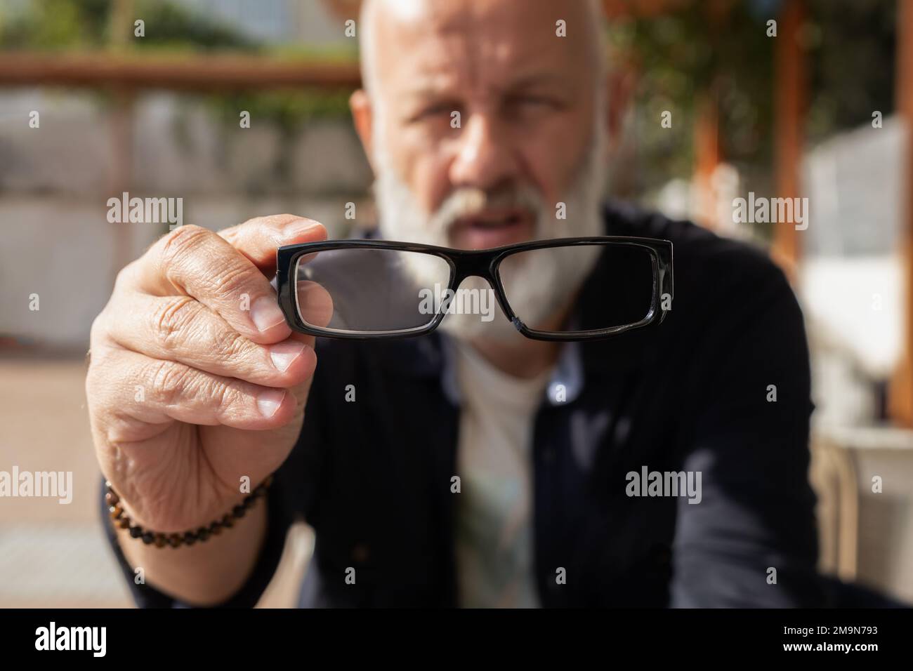un homme adulte avec une barbe grise regarde les lunettes cassées, effectue une mise au point sélective Banque D'Images
