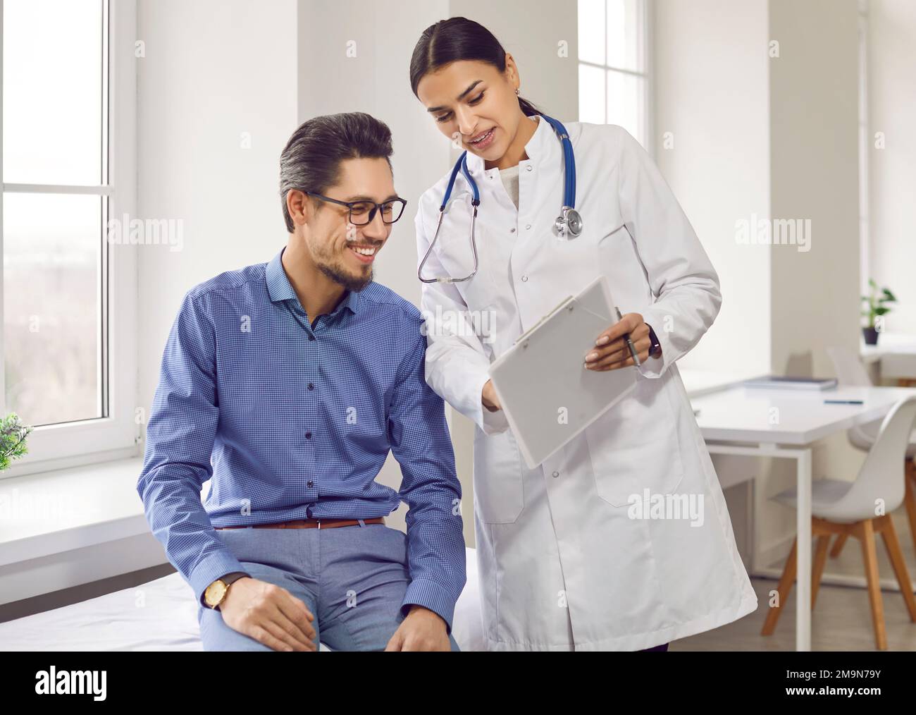 Une femme médecin professionnelle sourit et montre des résultats d'examen positifs à un homme jeune et joyeux. Banque D'Images