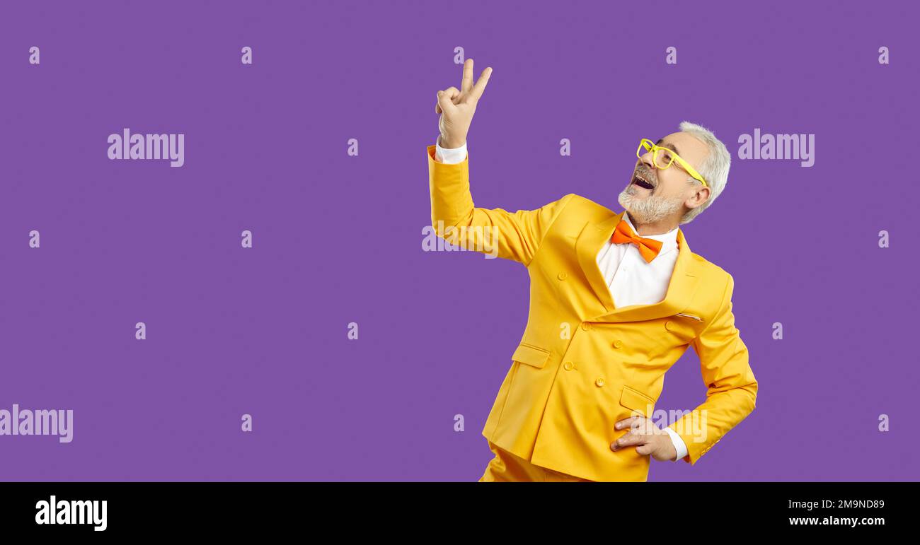 Portrait d'un homme aux cheveux gris gaie montrant un double signe en V isolé sur un arrière-plan violet vif et éclatant. Banque D'Images